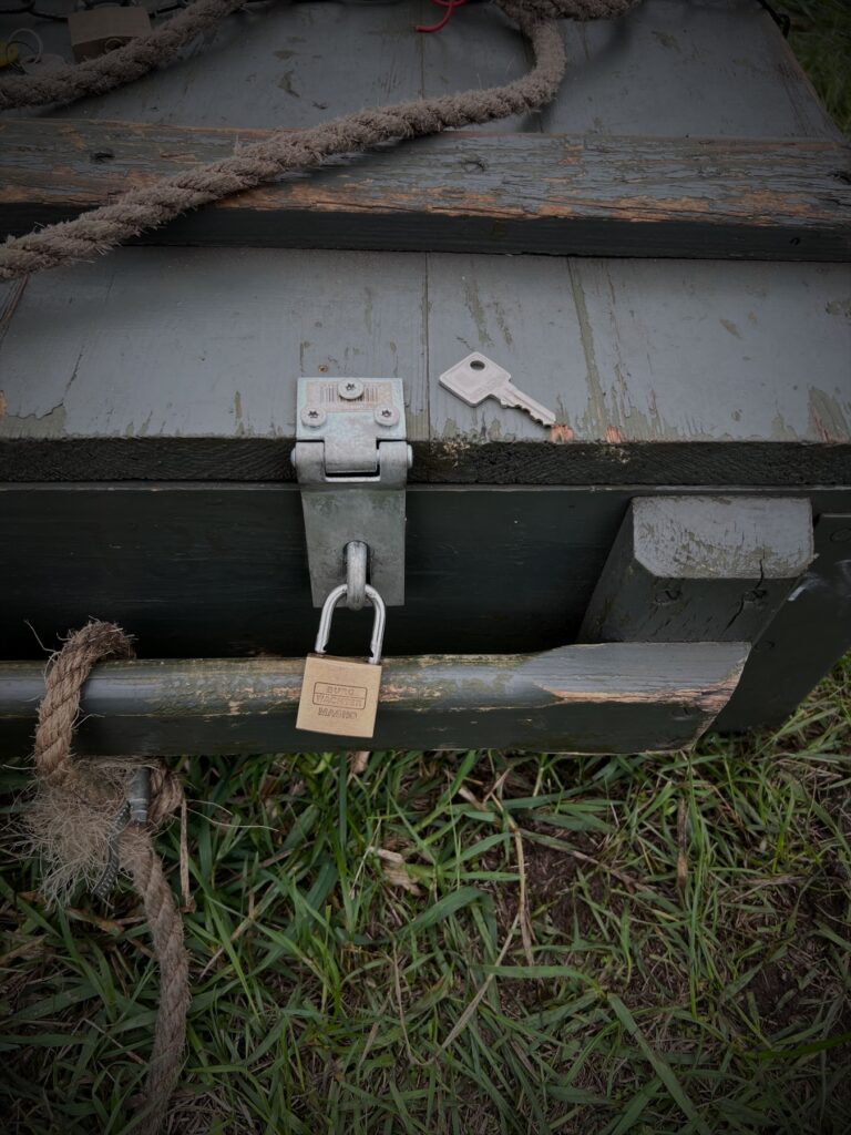 Platte legergroene kist met touw, hangslot en sleutel in het gras bij Red Alert